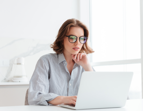 charming-businesswoman-in-glasses-and-striped-shirt-working-with-laptop-computer-while-siting-at-home 1